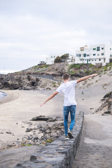 Rückenansicht eines jungen Mannes, der auf einer Mauer am Strand balanciert - SIPF01272