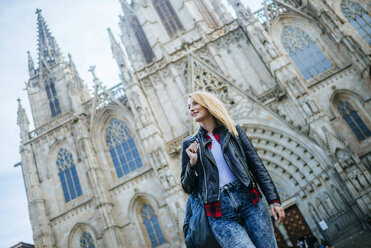 Spanien, Barcelona, lächelnde junge Frau, die vor einer Kathedrale spazieren geht - KIJF01039