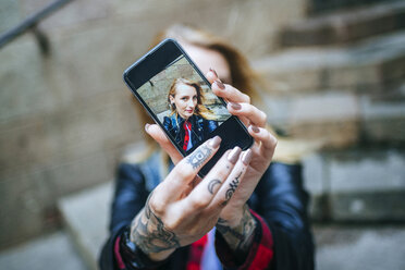 Tattooed woman's hands taking selfie with smartphone, close-up - KIJF01045