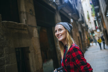 Spanien, Barcelona, Porträt einer lächelnden jungen Frau mit Kamera im Gotischen Viertel - KIJF01061