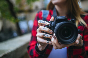 Tattooed woman's hands holding reflex camera, close-up - KIJF01064