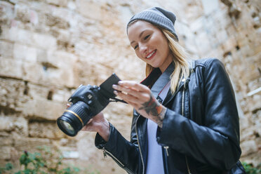 Lächelnde junge Frau, die sich Fotos auf ihrer Kamera ansieht - KIJF01069