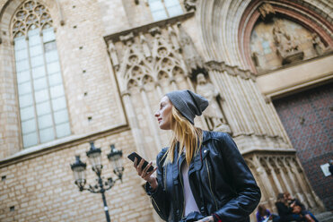 Spanien, Barcelona, junge Frau mit Mobiltelefon, die etwas beobachtet - KIJF01072