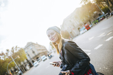 Spain, Barcelona, smiling young woman with mobile phone on the street - KIJF01073