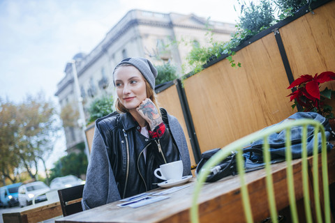 Junge tätowierte Frau sitzt in einem Straßencafé, lizenzfreies Stockfoto