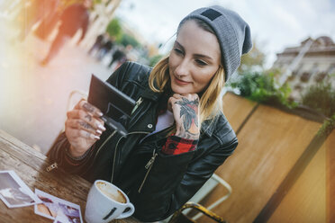 Young tattooed woman sitting in a pavement cafe looking at photos - KIJF01078