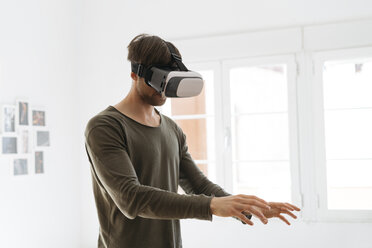 Young man wearing virtual reality glasses at home - KKAF00298