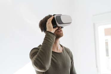Junger Mann trägt Virtual-Reality-Brille zu Hause - KKAF00299