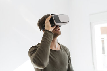 Young man wearing virtual reality glasses at home - KKAF00299