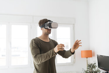 Young man wearing virtual reality glasses at home - KKAF00300