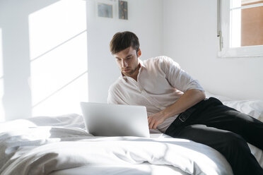 Young man lying on bed using laptop - KKAF00304