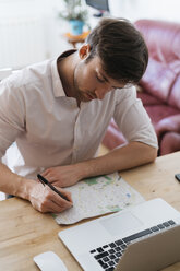 Junger Mann mit Stadtplan und Laptop zu Hause - KKAF00306