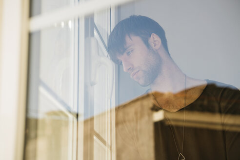 Sad young man looking through window - KKAF00308