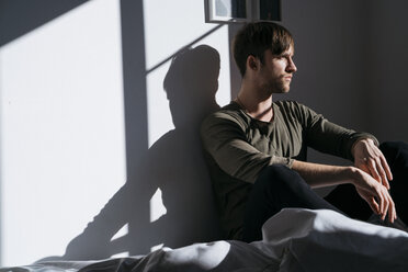 Serious young man sitting on bed at home - KKAF00311