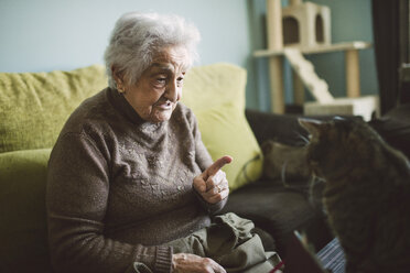 Senior woman sitting on the couch scolding her cat - RAEF01633