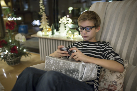 Gift giving at Christmas eve, boy paying with smart phone having present on his lap stock photo