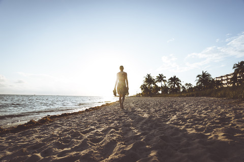 USA, Florida, Key West, Frau geht bei Sonnenuntergang am Strand spazieren, lizenzfreies Stockfoto