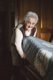Ältere Frau legt frische Laken auf ein Bett - RAEF01642