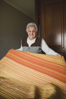 Ältere Frau legt frische Laken auf ein Bett - RAEF01644