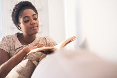 Junge Frau sitzt auf der Couch und liest ein Buch - SIPF01292