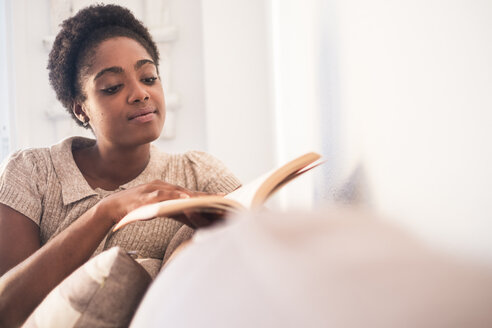 Junge Frau sitzt auf der Couch und liest ein Buch - SIPF01292