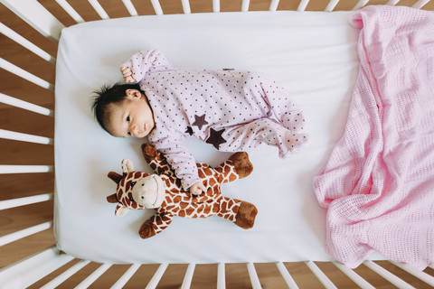 Neugeborenes Mädchen in der Krippe liegend mit einer Plüschgiraffe, lizenzfreies Stockfoto