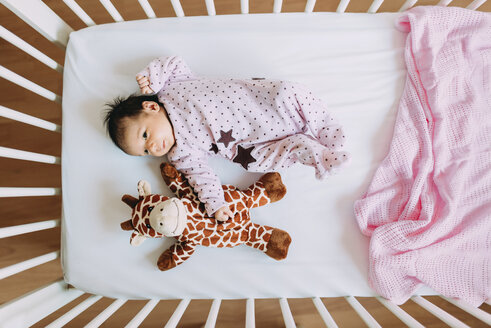 Neugeborenes Mädchen in der Krippe liegend mit einer Plüschgiraffe - GEMF01380
