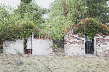 Bride and groom standing seperated in brick huts - ASCF00685