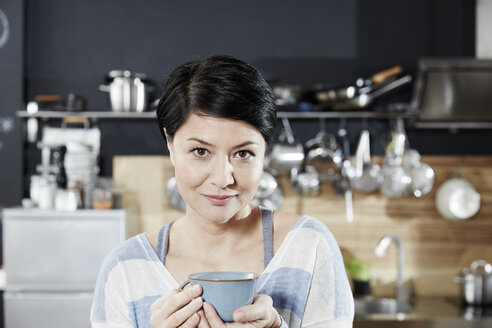 Portrait of woman in kitchen with cup of coffee - FMKF03458