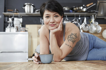 Porträt einer lächelnden Frau in der Küche mit einer Tasse Kaffee - FMKF03463