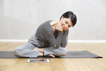 Lächelnde Frau auf Yogamatte sitzend mit Tablet - FMKF03473