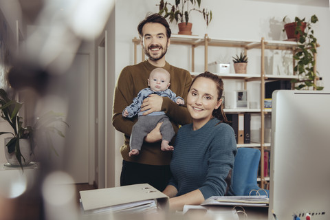 Portrait of smiling father and mother with baby in home office stock photo