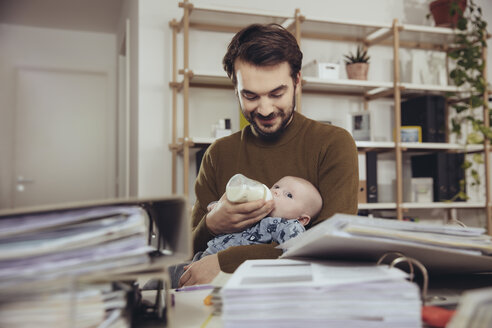 Father feeding his baby in home office - MFF03429