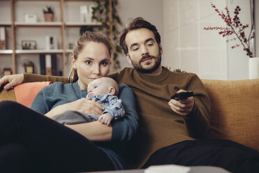 Vater und Mutter sitzen mit Baby auf der Couch und sehen fern - MFF03433