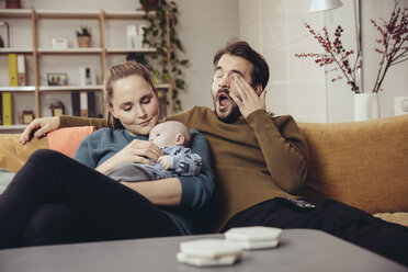 Müder Vater und Mutter sitzen mit Baby auf der Couch - MFF03434