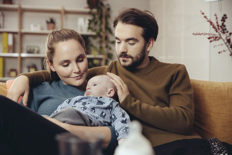 Father and mother cuddling with baby on couch stock photo