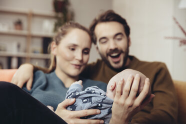 Vater und Mutter betrachten das Baby auf der Couch - MFF03436