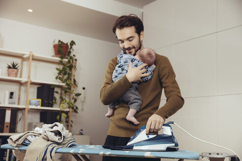 Father ironing and holding his baby at home - MFF03437