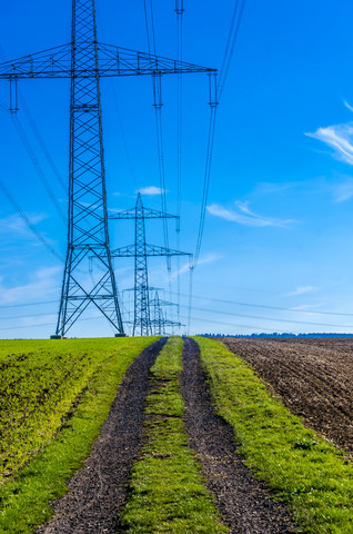 Row of high-voltage poles with dirt track in the foreground stock photo