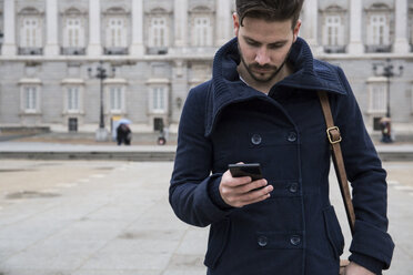 Mann mit Mantel und Tasche benutzt sein Telefon - ABZF01792