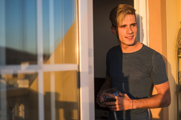 Portrait of smiling young man with glass of red wine on balcony at sunset - SIPF01305