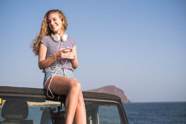 Junge Frau sitzt auf Auto am Strand - SIPF01310