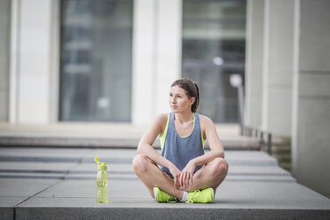 Sportliche Frau mit Trinkflasche auf dem Boden sitzend - ASCF00715