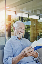 Älterer Mann sitzt auf der Terrasse und liest ein Buch - RORF00439