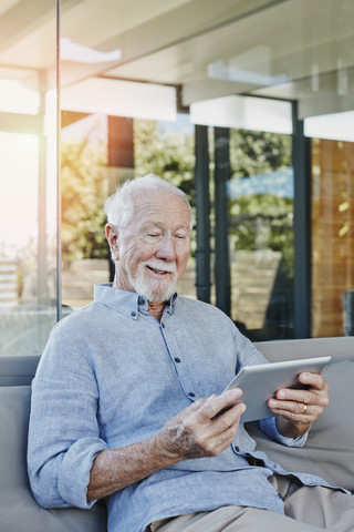 Älterer Mann sitzt auf der Terrasse und liest ein ebook, lizenzfreies Stockfoto