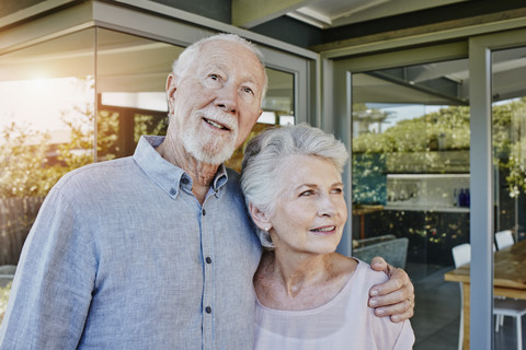 Ein älteres Ehepaar steht vor seinem Haus und sieht zuversichtlich aus, lizenzfreies Stockfoto