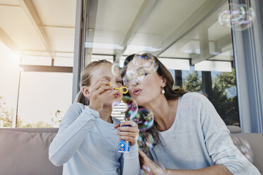 Mutter und Tochter blasen Seifenblasen auf der Terrasse - RORF00506
