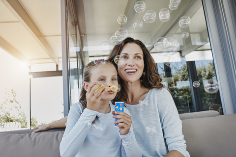 Mother and daughter blowing soap bubbles on terrace stock photo