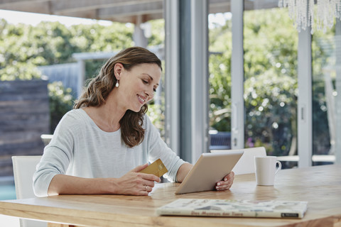 Frau, die auf der Terrasse sitzt und eine Online-Zahlung mit Kreditkarte vornimmt, lizenzfreies Stockfoto