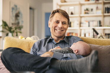 Lächelnder Vater und sein neugeborenes Baby sitzen auf der Couch zu Hause - MFF03460